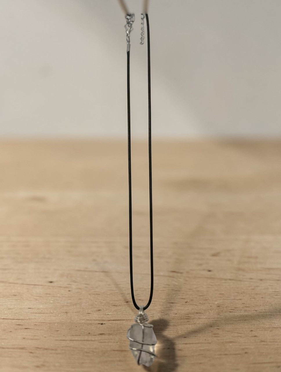 Clear quartz necklace featuring a handmade wire wrapped raw crystal pendant on a black chain.