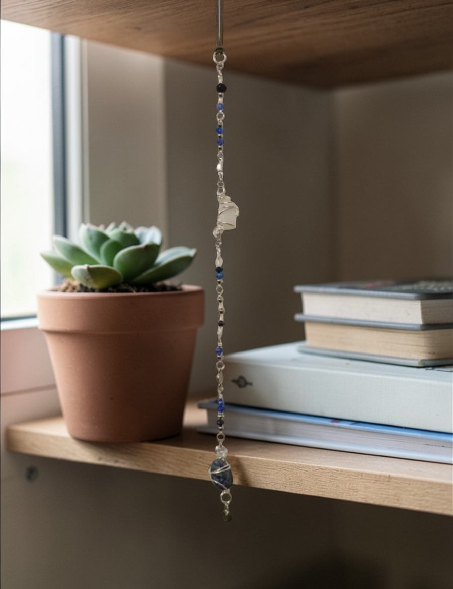 Sodalite suncatcher hanging next to a potted succulent on a shelf, showcasing handmade blue crystal beads.